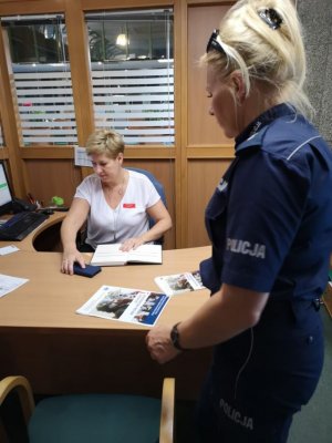 na zdjęciu policjantka w umundurowaniu służbowym przekazująca pracownicy banku ulotki informujące o oszustwach seniorów