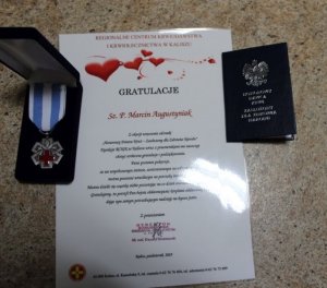 Zdjęcie kolorowe, na nim dyplom Regionalnego Centrum  Krwiodawstwa i Krwiolecznictwa w Kaliszu dla sierż. szt. Marcina Augustyniaka, legitymacja Honorowego Dawcy Krwi - Zasłużonego Dla Zdrowia Narodu oraz medal