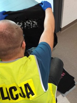 zdjęcie kolorowe na zdjęciu policjant operacyjny trzymający odzież z podrobionymi znakami towarowymi