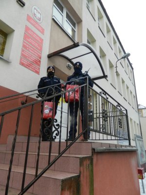 Zdjęcie kolorowe. Umundurowani policjanci stojący  na schodach Urzędu Gminy w Opatówku